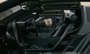Close-up side view of several black DeLorean cars lined up in a row, focusing on their open gull-wing doors and minimalist black leather interiors, creating a futuristic and uniform aesthetic